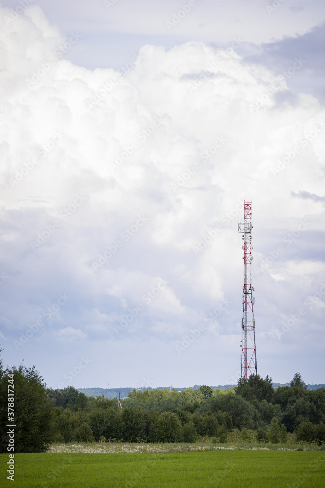 A telecommunications tower with radio and satellite dishes is installed in a rural area on a green field surrounded by trees. The concept of the harmlessness of electromagnetic and microwave A telecommunications tower with radio and satellite dishes is installed in a rural area on a green field surrounded by trees. The concept of the harmlessness of electromagnetic and microwave