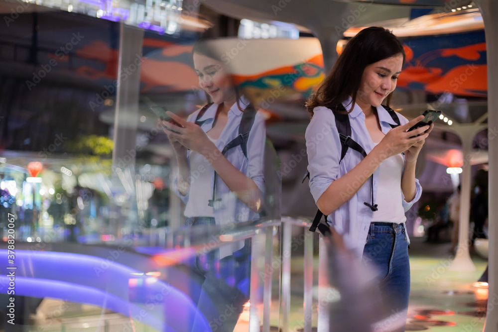 Fototapeta premium Beautiful women using smartphone in the city in night time with reflect on the mirror.