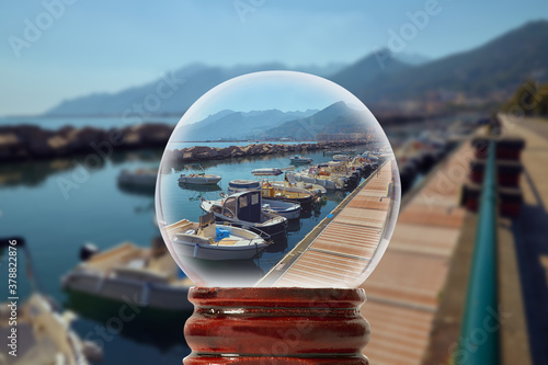 Small dock in Italy for boats and yachts with mountains on the background through a glass transparent ball 