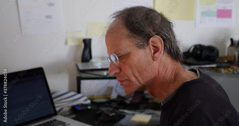 A teacher in a messy school office giving an online remote class to his students via a video livestream during a pandemic. A teacher in a messy school office giving an online remote class to his students via a video livestream during a pandemic.