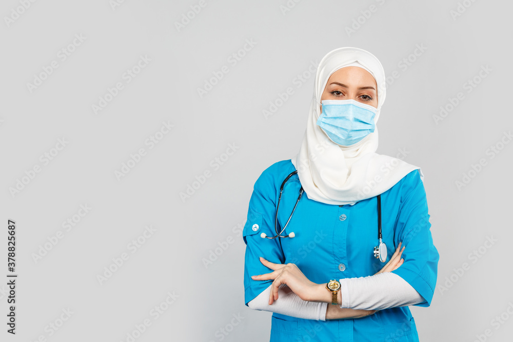 friendly Muslim doctor or nurse wearing hijab and medical face mask and gloves on a gray background. friendly Muslim doctor or nurse wearing hijab and medical face mask and gloves on a gray background.