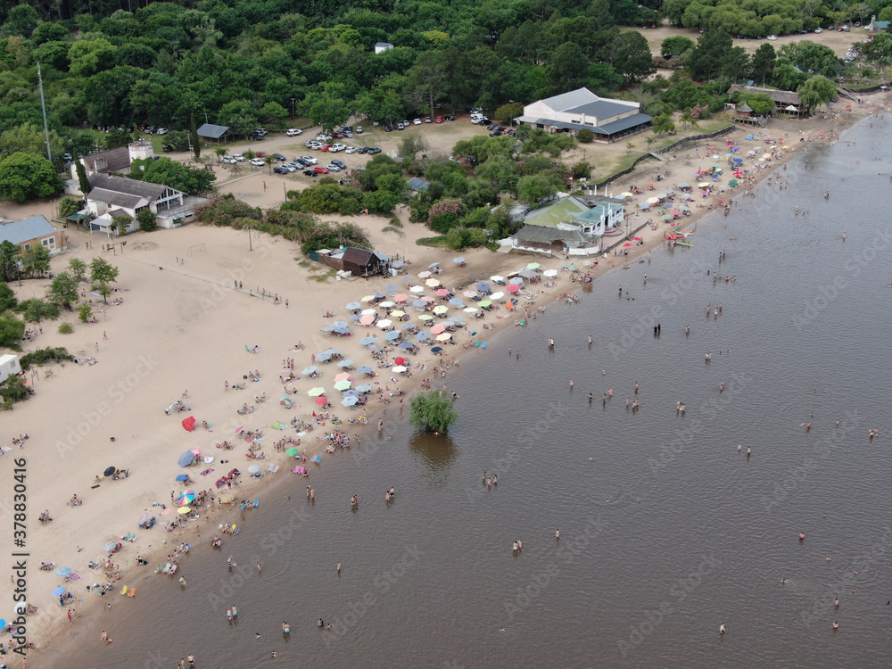 La costa de un río, con gente descansando y sombrillas en la arena de la playa.