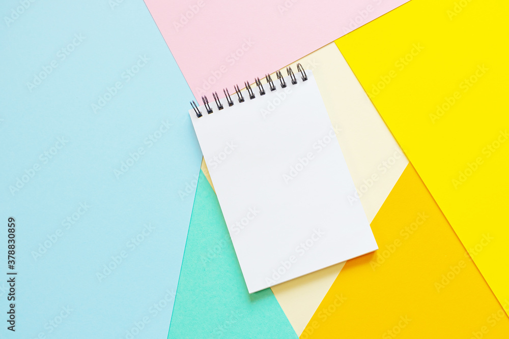 Spiral notebook with blank white sheet on multi-colored paper. The concept of office, school, creativity, learning. Top view, flat lay, copy space, minimalism. Pink, blue, orange and yellow shades. Spiral notebook with blank white sheet on multi-colored paper. The concept of office, school, creativity, learning. Top view, flat lay, copy space, minimalism. Pink, blue, orange and yellow shades.