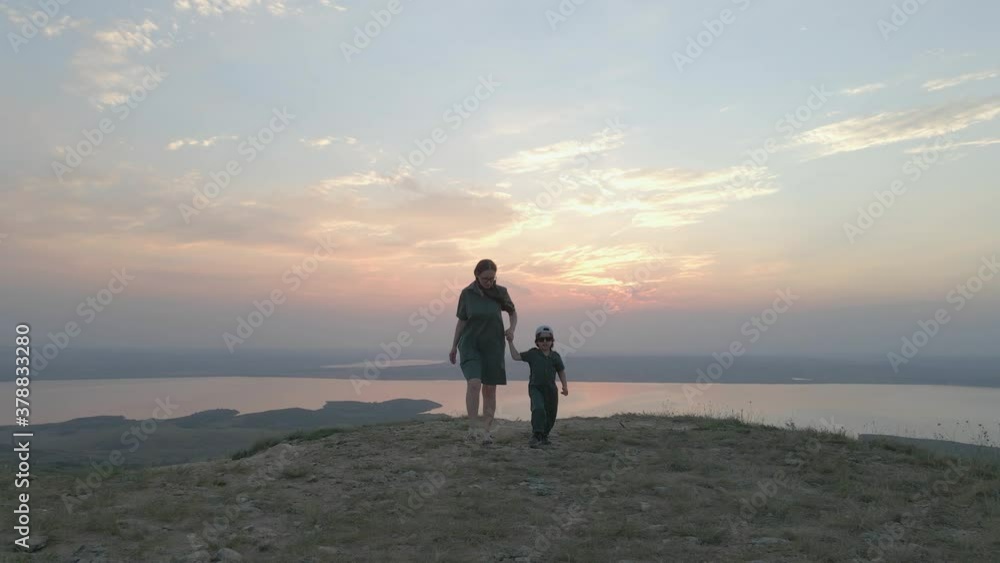 mother and son walking on the mountain in green linen clothes in summer at sunset on the background of the lake captured on a drone mother and son walking on the mountain in green linen clothes in summer at sunset on the background of the lake captured on a drone