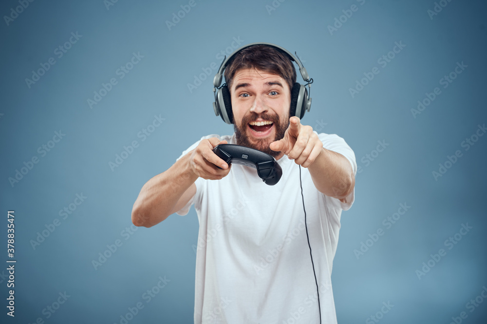 Man in headphones controller in hands playing game console lifestyle emotions blue background white t-shirt Man in headphones controller in hands playing game console lifestyle emotions blue background white t-shirt