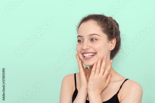 The girl smiles, touches her face with her hands.