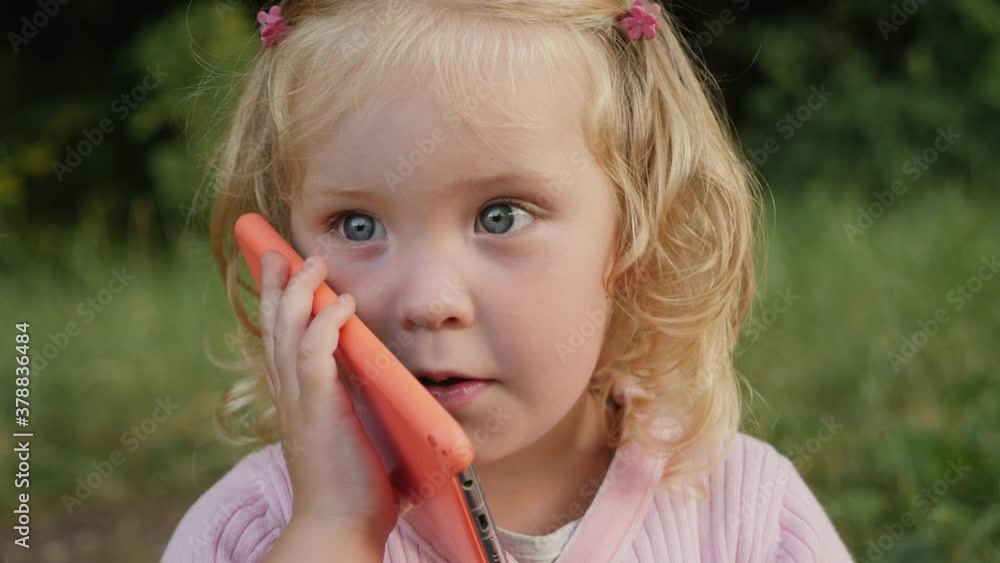 Cute little girl calls by mobile phone and fun talks. Child grimaces, communicates on a smartphone Cute little girl calls by mobile phone and fun talks. Child grimaces, communicates on a smartphone