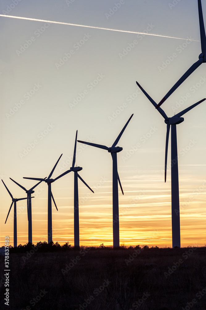 Fototapeta premium Wind Turbines at Dusk. Landscape sunset with windmills. Renewal source of electricity. Wind turbines field new technology for clean energy on mountain, sunset view with colorful twilight on sky.