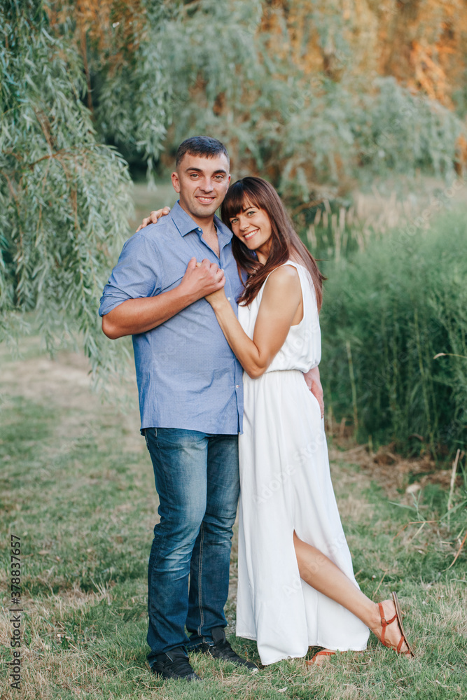 Fototapeta premium Beautiful smiling couple man woman in love. Husband and wife hugging in park on summer day at sunset. Togetherness and happiness. Authentic real people family outdoors.