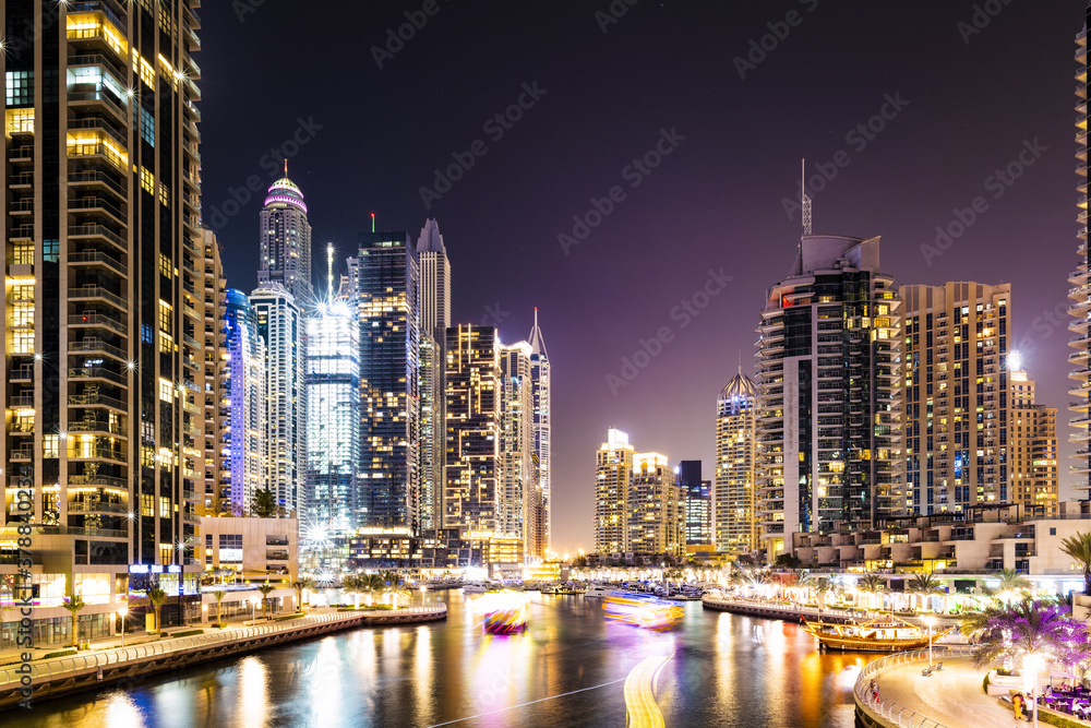 Stunning view of the Dubai Marina at dusk with illuminated skyscrapers in the background and light trails left by some boats sailing in the water canal. Dubai, United Arab Emirates.