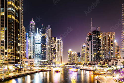 Stunning view of the Dubai Marina at dusk with illuminated skyscrapers in the background and light trails left by some boats sailing in the water canal. Dubai  United Arab Emirates.