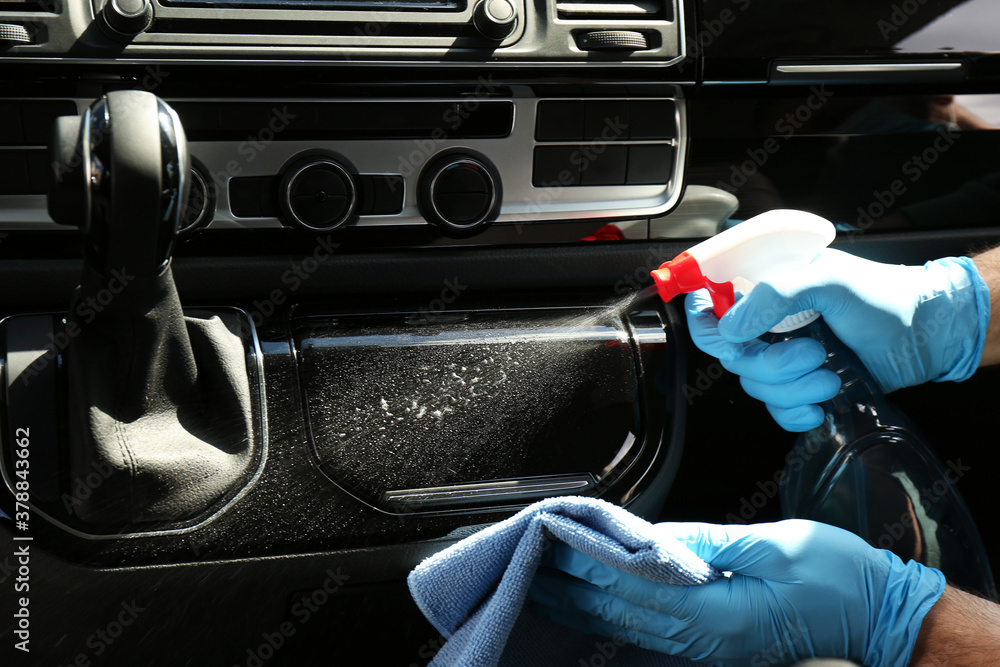 Man in gloves cleaning car dashboard with disinfectant spray and rag