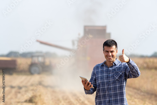 Quadro em tela Farmer with tablet in front of combine harvester in soybean field