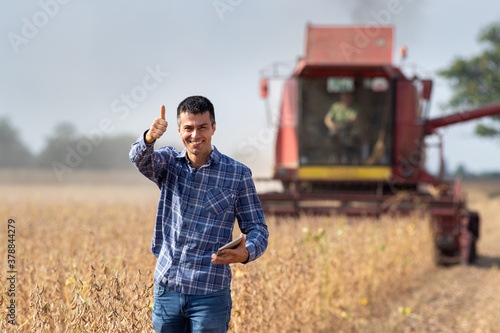 Wall Mural Farmer with tablet in front of combine harvester in soybean field