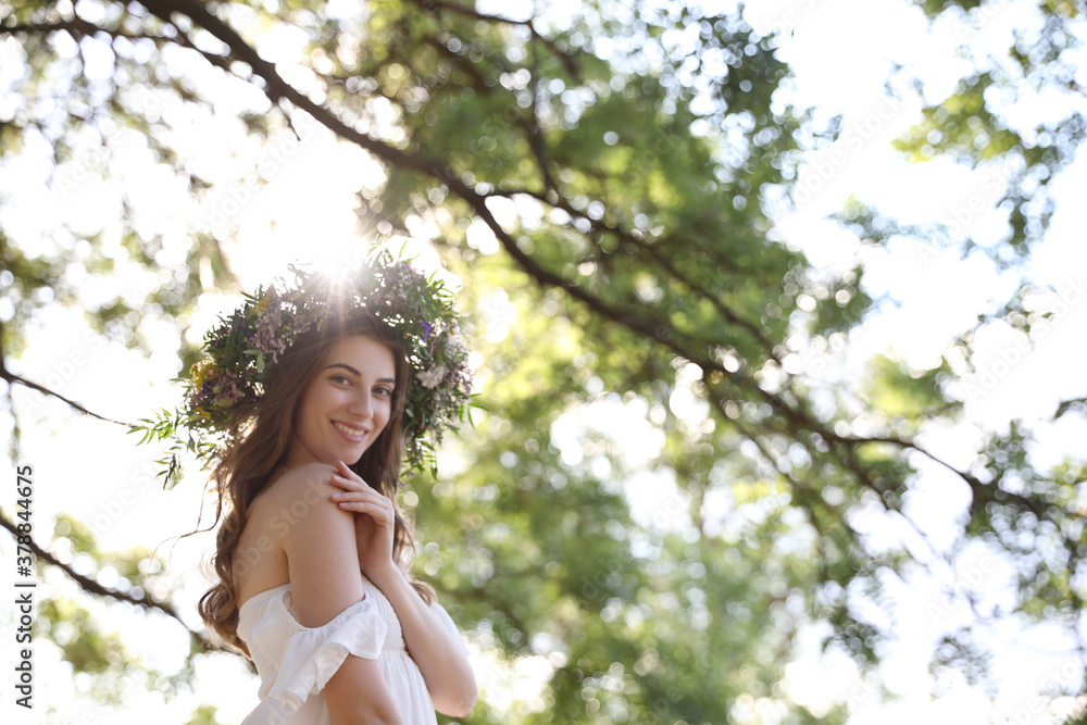 Young woman wearing wreath made of beautiful flowers outdoors on sunny day Young woman wearing wreath made of beautiful flowers outdoors on sunny day
