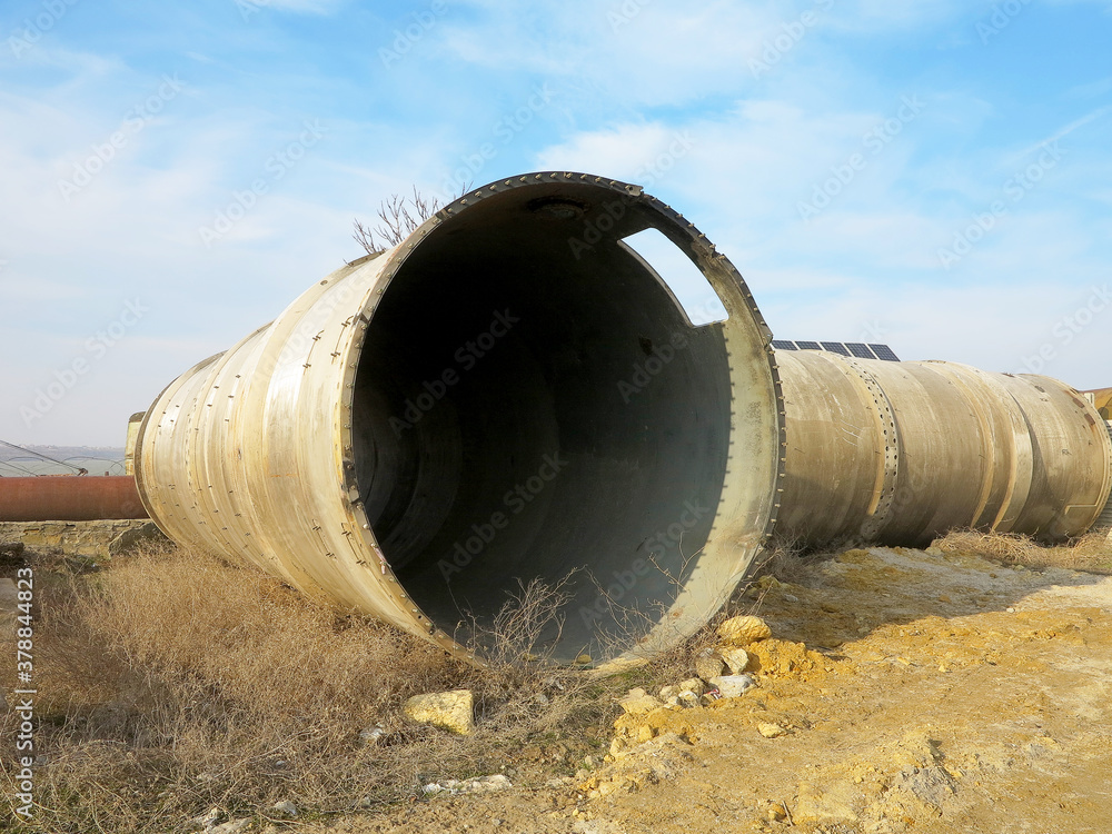 Old rye pipes of large diameter lie on the ground. Pipeline. Large iron drainage pipes connect two reservoirs. Large diameter metal pipe for agricultural irrigation system.