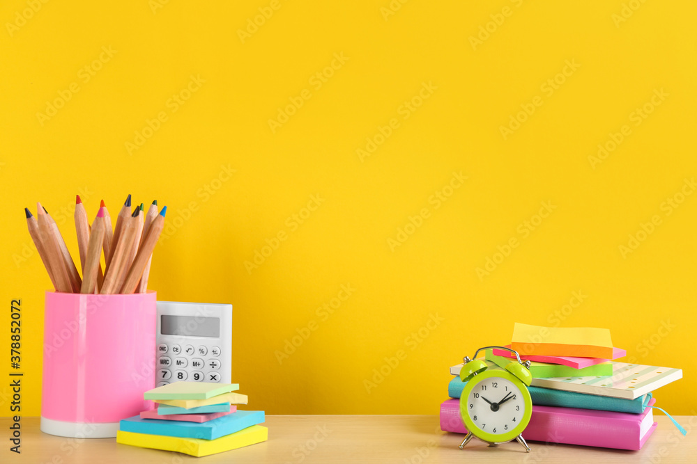 Fototapeta premium Different school stationery and alarm clock on table against yellow background, space for text. Back to school