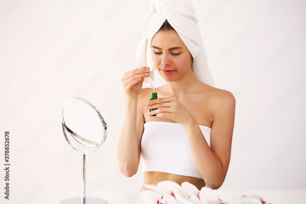 Young brunette girl takes care of her skin, standing in front of a mirror, enjoying beauty treatments for herself, smiling tenderly Young brunette girl takes care of her skin, standing in front of a mirror, enjoying beauty treatments for herself, smiling tenderly