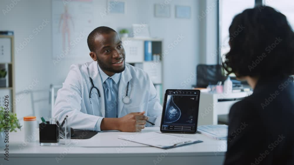 African American Medical Doctor Showing Mammography Test Results to a Patient on a Tablet Computer in a Health Clinic. Friendly Assistant Explains Importance of Breast Cancer Prevention Screening. African American Medical Doctor Showing Mammography Test Results to a Patient on a Tablet Computer in a Health Clinic. Friendly Assistant Explains Importance of Breast Cancer Prevention Screening.
