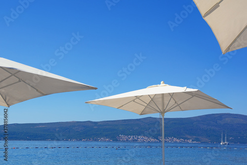 Beach vacation concept. White sun umbrellas against blue sky. Montenegro  Adriatic Sea. View of Kotor Bay near Tivat city