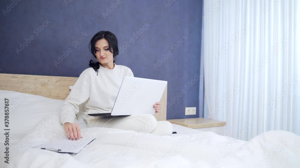 young sick business woman manager working at home in bed during illness. Female in white pajamas or a sports suit works on the sofa in the morning with a laptop and documents. businesswoman in bedroom young sick business woman manager working at home in bed during illness. Female in white pajamas or a sports suit works on the sofa in the morning with a laptop and documents. businesswoman in bedroom