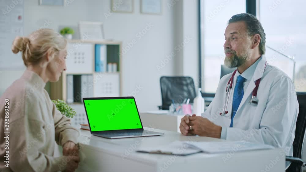 Family Medical Doctor is Explaining Diagnosis to a Senior Patient on a Computer with Green Screen in a Health Clinic. Assistant in White Lab Coat is Reading Medical History in Hospital Office. Family Medical Doctor is Explaining Diagnosis to a Senior Patient on a Computer with Green Screen in a Health Clinic. Assistant in White Lab Coat is Reading Medical History in Hospital Office.