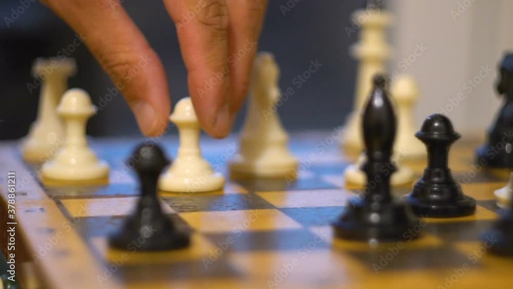 A man's hand moves a chess piece. Board game. Black and white pieces. White pawn. Strategic solution. Business thinking. Close-up. A man's hand moves a chess piece. Board game. Black and white pieces. White pawn. Strategic solution. Business thinking. Close-up.