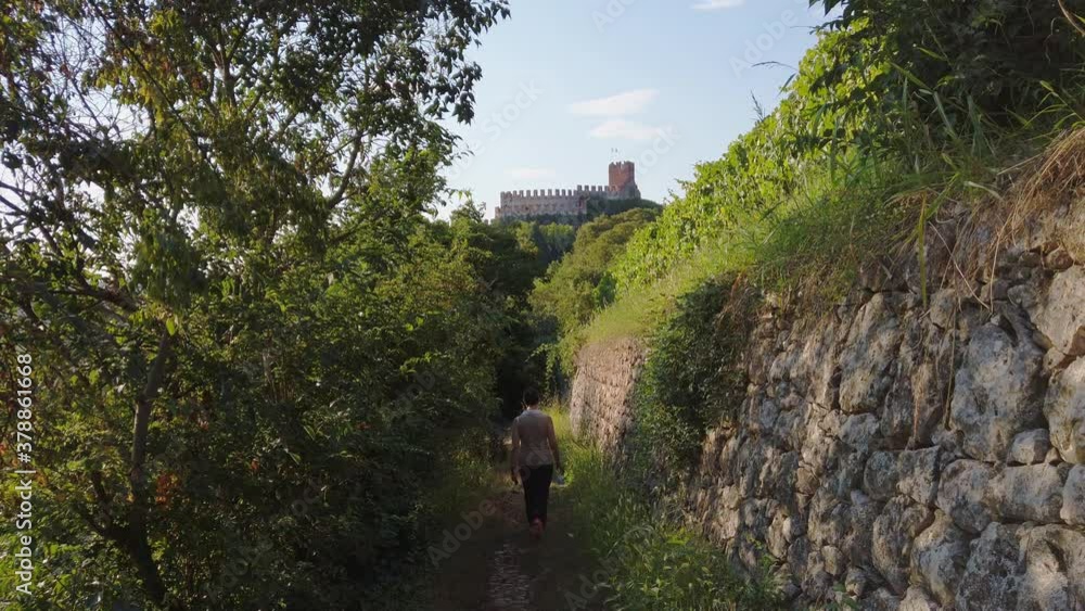 Woman hiking along a nature trail going toward the castle of Soave, Italy Woman hiking along a nature trail going toward the castle of Soave, Italy