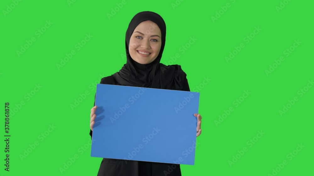 Smiling Arab woman in hijab holding blank blue poster and looking at camera on a Green Screen, Chroma Key. Smiling Arab woman in hijab holding blank blue poster and looking at camera on a Green Screen, Chroma Key.