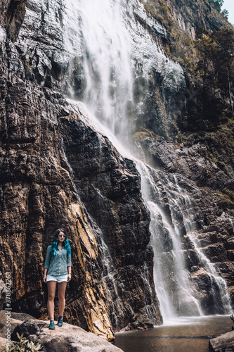 Young blue haired girl standing under Diyaluma waterfall in Sri Lanka. White tourist in Asia enjoying vacation during high season. Adventure traveler exploring the world. Beautiful outdoor picture. photo