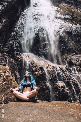 Young Caucasian girl under Diyaluma waterfall, Sri Lanka. Happy woman in meditation pose on vacation. Wellness lifestyle, healthy yoga retreat in summer. Peaceful holiday in beautiful exotic place