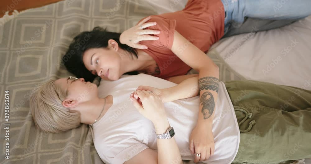 Joyful blonde lesbian lies on designed carpet and hugs girlfriend with dark loose flowing hair smiling slow motion upper view Joyful blonde lesbian lies on designed carpet and hugs girlfriend with dark loose flowing hair smiling slow motion upper view