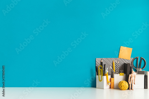 Creative desk with a blank picture frame or poster, desk objects, office supplies, books, and plant on a blue background.	
