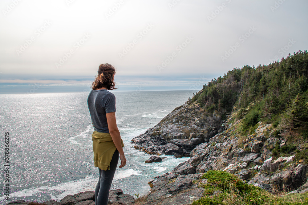 Woman looking at a rocky coast by the edge of the ocean in summer