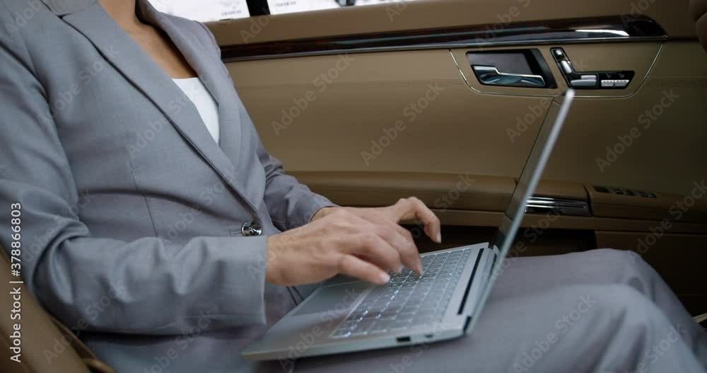 Caucasian businesswoman sitting on backseat of car and working on laptop computer. Beautiful woman typing on keyboard while going to work. Busy female rich entrepreneur texting email by way o office. Caucasian businesswoman sitting on backseat of car and working on laptop computer. Beautiful woman typing on keyboard while going to work. Busy female rich entrepreneur texting email by way o office.