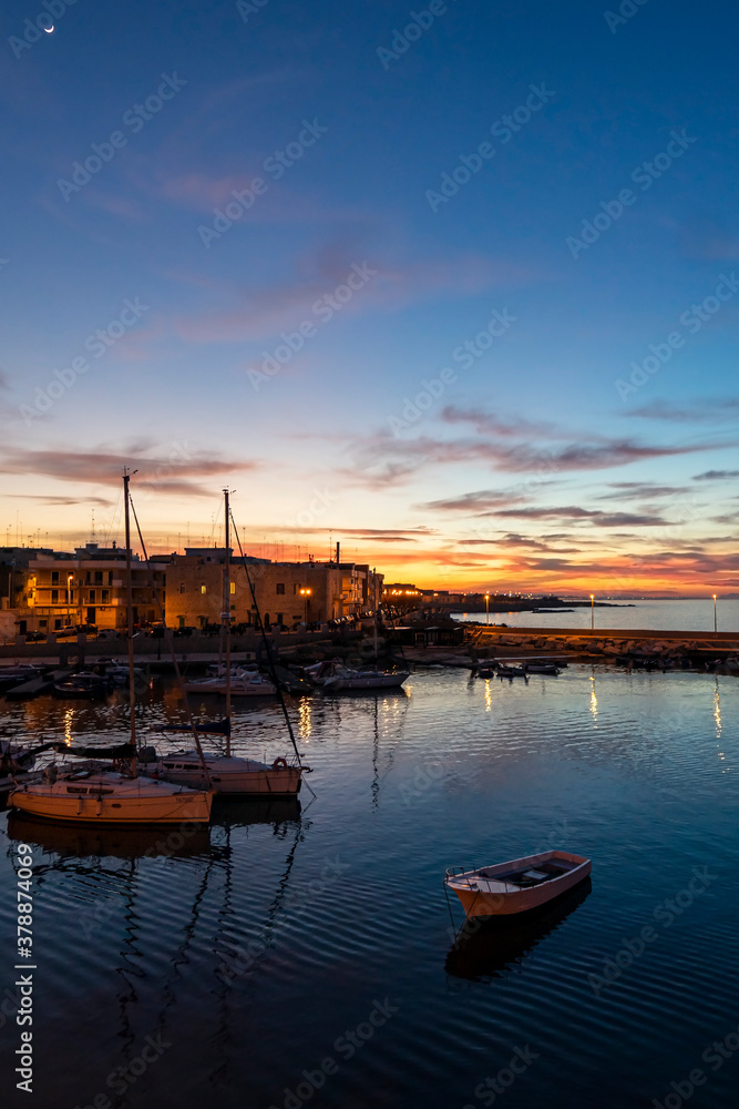 The port with boats with one lonely separated, small, wooden boat at sunset with a moon. Giovinazzo, Metropolitan City of Bari, Apulia region, southeastern Italy.