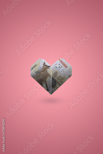 Coração feito com cédula brasileira de 200 reais em um fundo rosa. photo