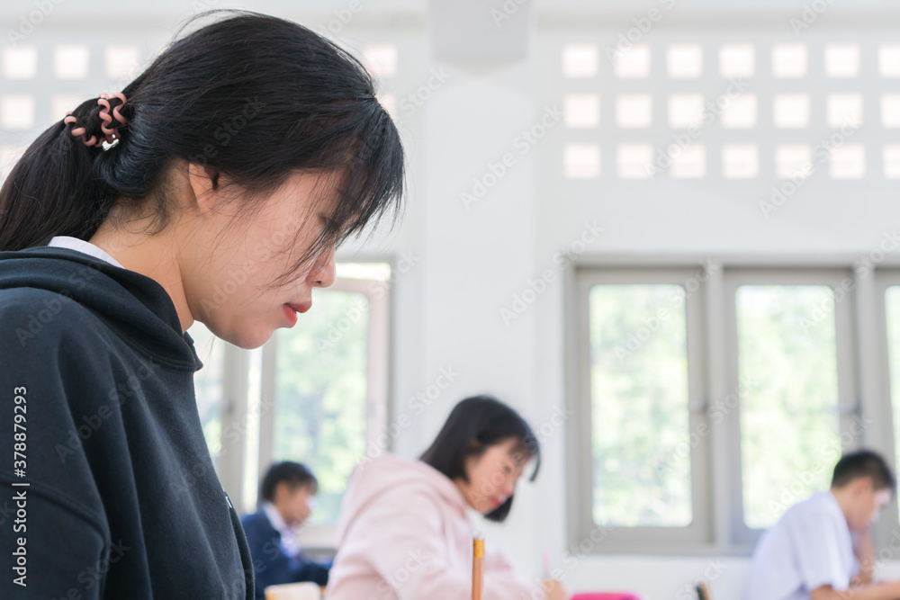 Asian High school or university student reading question exam test class and using pencil writing on paper answer sheet, doing final exam attending in examination classroom with students in uniform Asian High school or university student reading question exam test class and using pencil writing on paper answer sheet, doing final exam attending in examination classroom with students in uniform