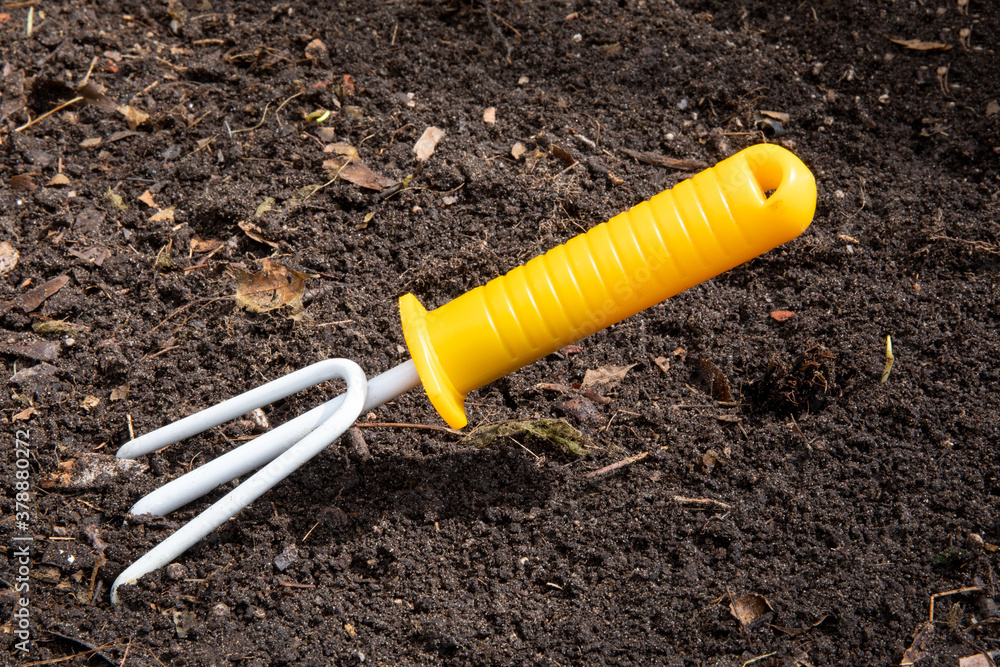 a yellow flower bed rake stuck into the earth to loosen it for planting a yellow flower bed rake stuck into the earth to loosen it for planting