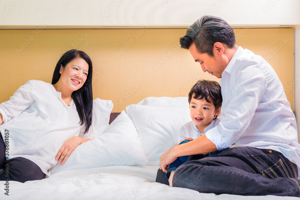 Friendly family. Asian family in white shirt are sharing good emotions while relaxing in bed together at home Friendly family. Asian family in white shirt are sharing good emotions while relaxing in bed together at home