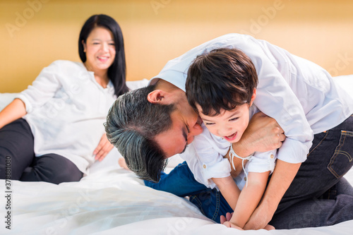 Asian Mother, father and their cute son resting together on bed in hotel room.