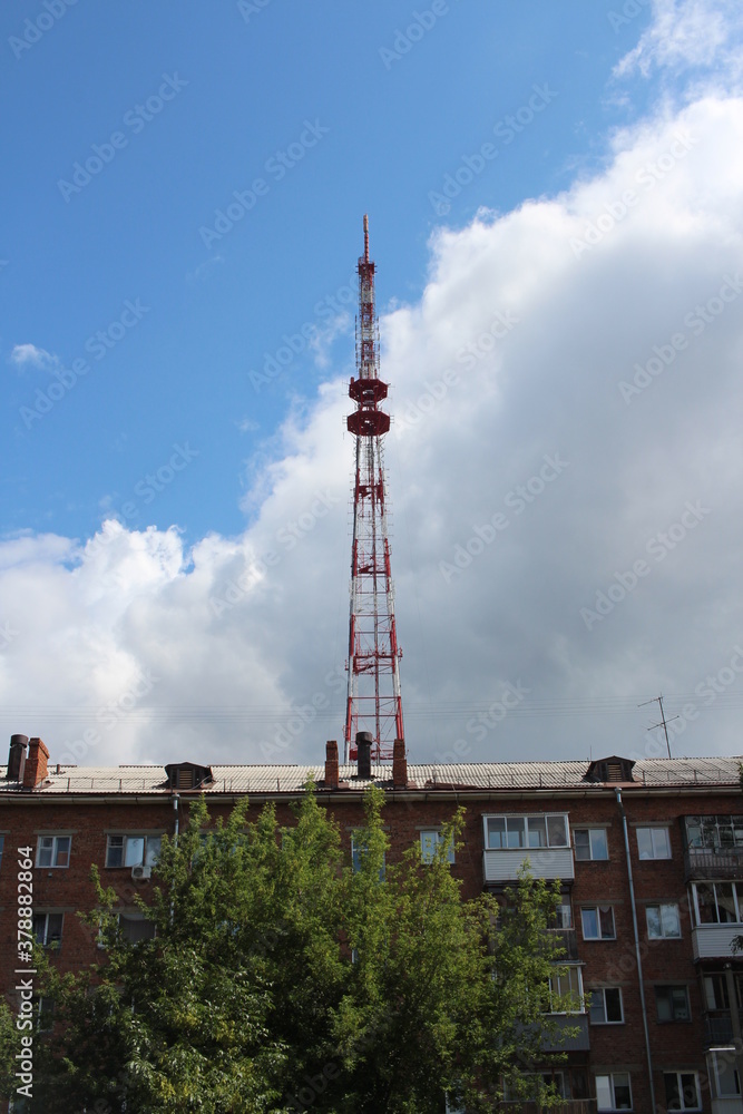 a high TV tower in the city above an apartment building emits radio signals