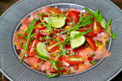 Smoked salmon carpaccio salad topped with capers, peppers, and rocket leaves.