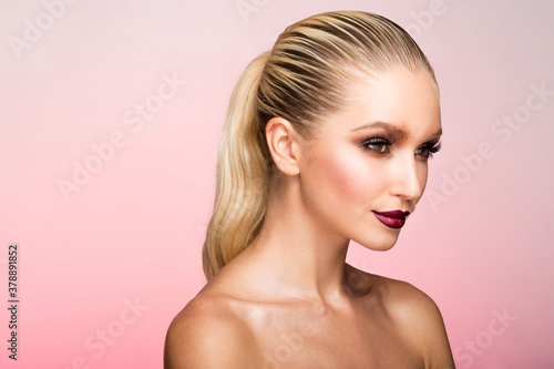 Closeup portrait of woman with splendid makeup and hair straightened and caught in the back, over pink background.