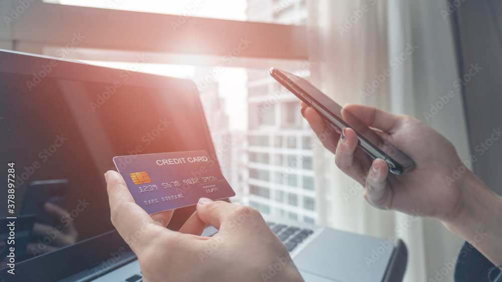 Woman hands holding a blue credit card and using a smartphone for shopping online or internet banking with laptop background. Online shopping concept. Woman hands holding a blue credit card and using a smartphone for shopping online or internet banking with laptop background. Online shopping concept.