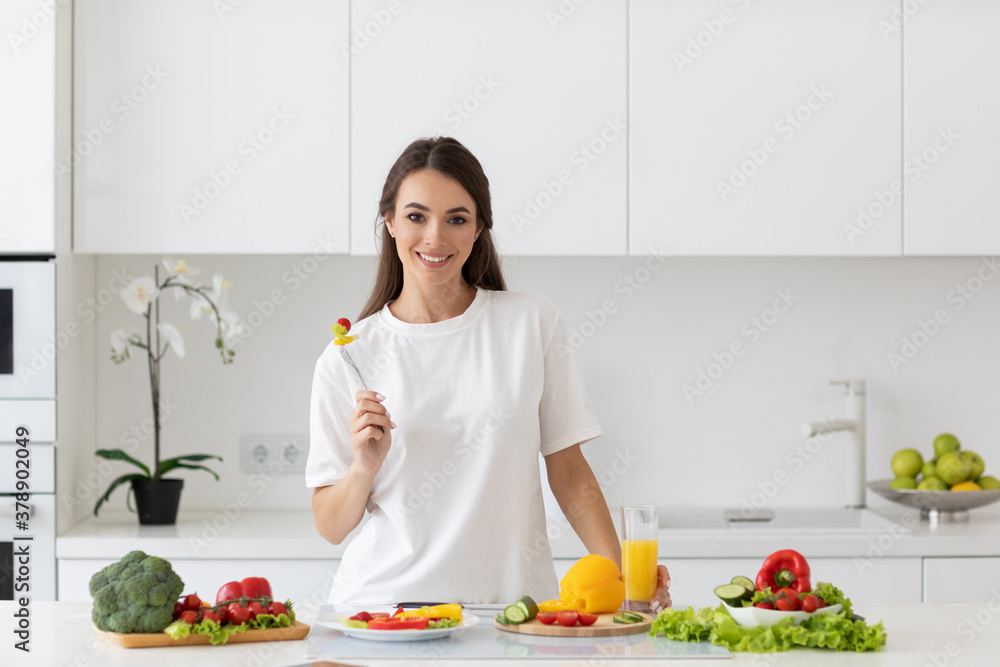 Young beautiful woman preparing a salad of fresh vegetables in a bright kitchen.