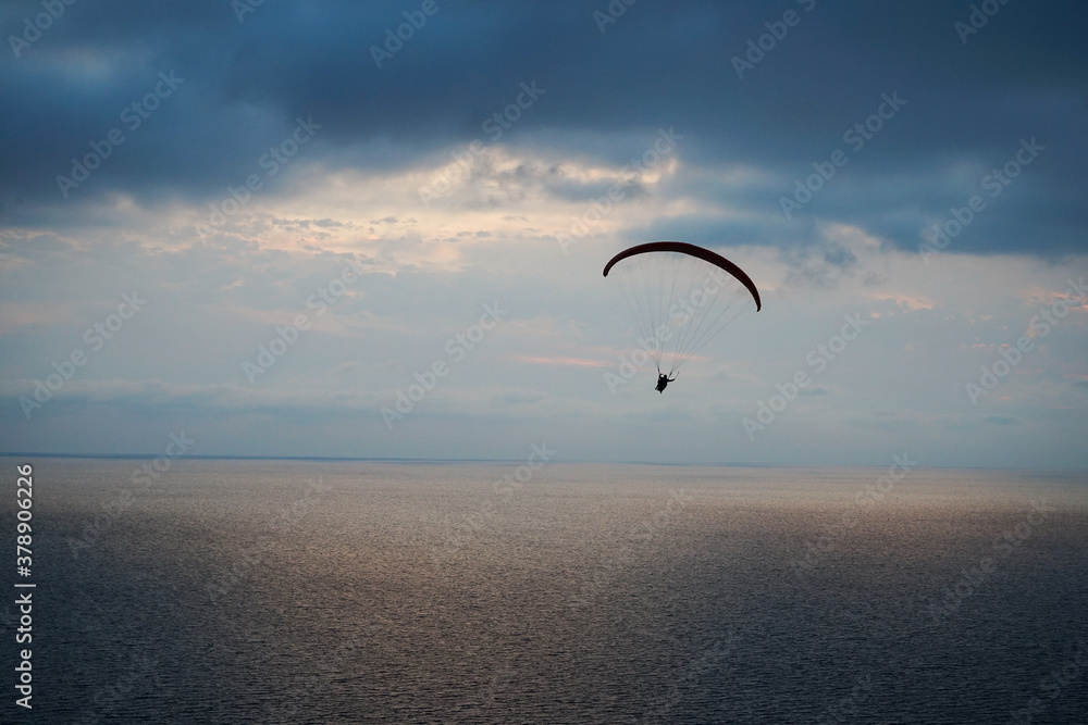 a paraglider flies over the sea at sunset against the background of the light part of the sky between the dark sea and dark clouds a paraglider flies over the sea at sunset against the background of the light part of the sky between the dark sea and dark clouds