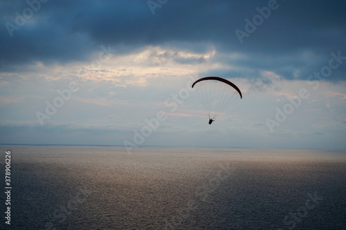 a paraglider flies over the sea at sunset against the background of the light part of the sky between the dark sea and dark clouds