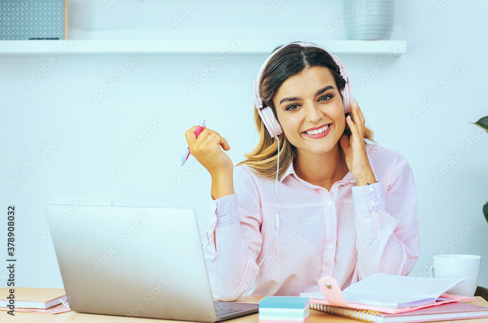 Portrait of a young female student smiling at camera while listening to online course Portrait of a young female student smiling at camera while listening to online course