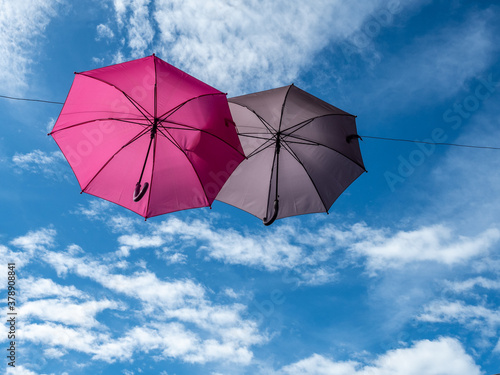Two decorative pink and grey umbrellas hanging on ropes in the air on blue sky background with clouds. Horizontal picture